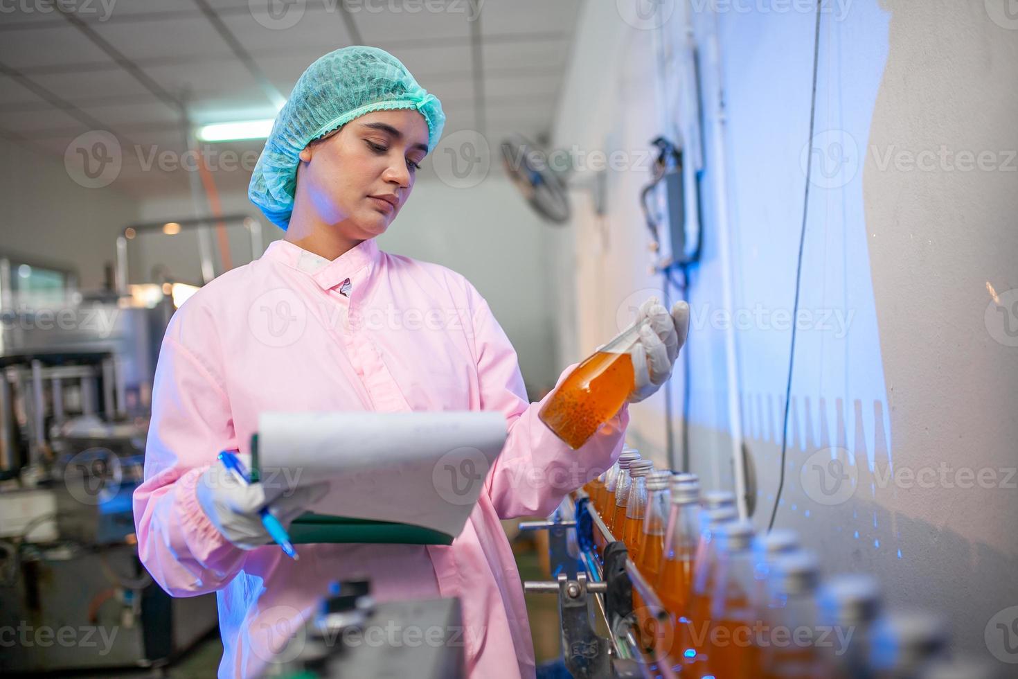 Asian woman worker with clipboard is checking product bottles of fruit juice on the production line in the beverage factory. Manufacturer checks quality of food industry. photo