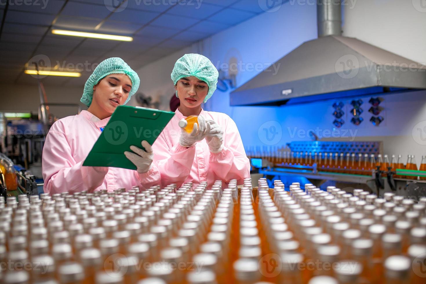 Asian woman worker with clipboard is checking product bottles of fruit juice on the production line in the beverage factory. Manufacturer checks quality of food industry. photo