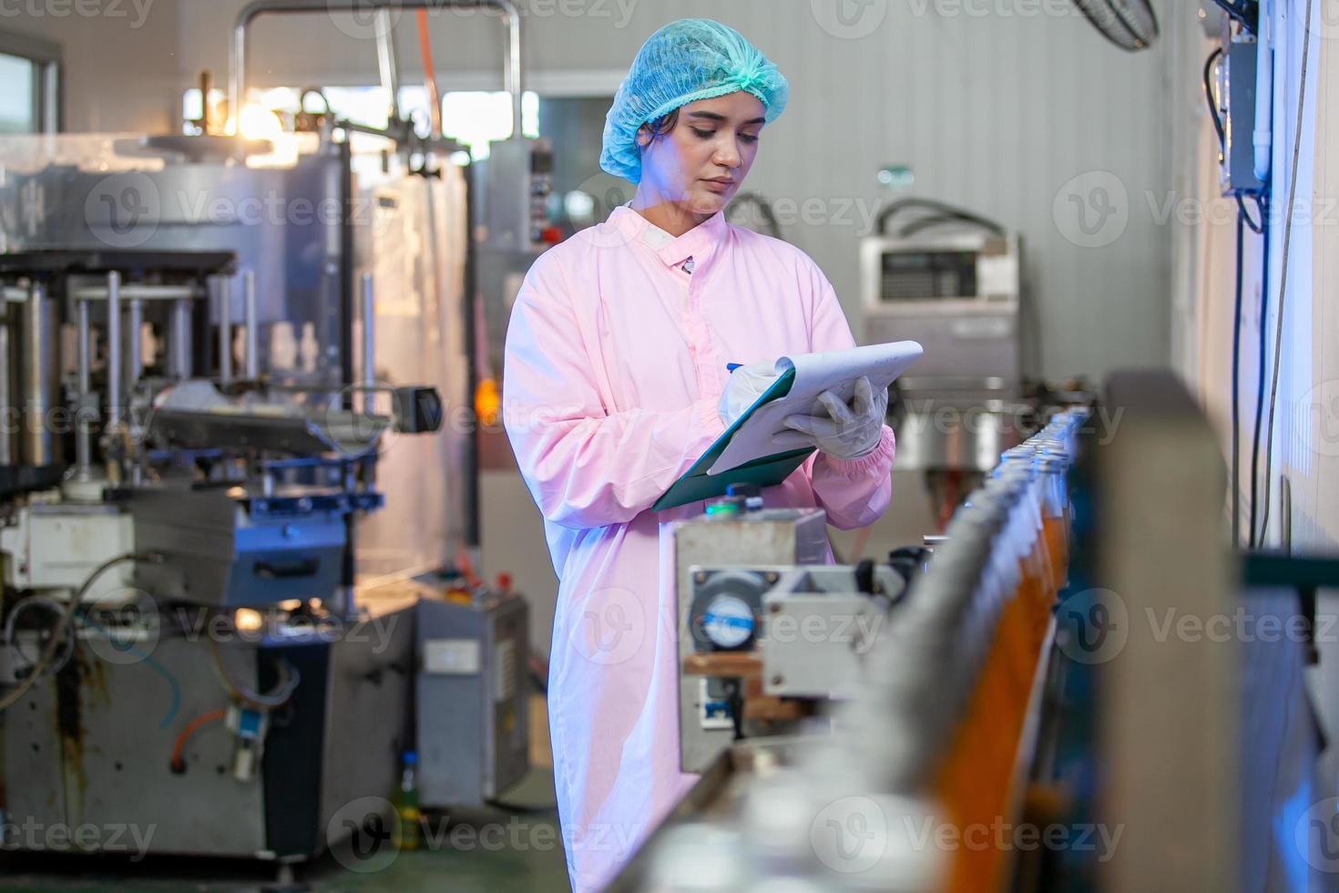 Asian woman worker with clipboard is checking product bottles of fruit juice on the production line in the beverage factory. Manufacturer checks quality of food industry. photo