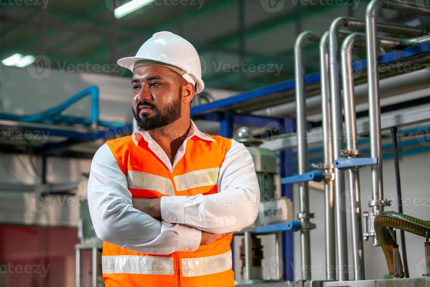 Professional engineer with helmet works to maintain industrial construction equipment. Worker is standing in the factory with their arms crossed. photo