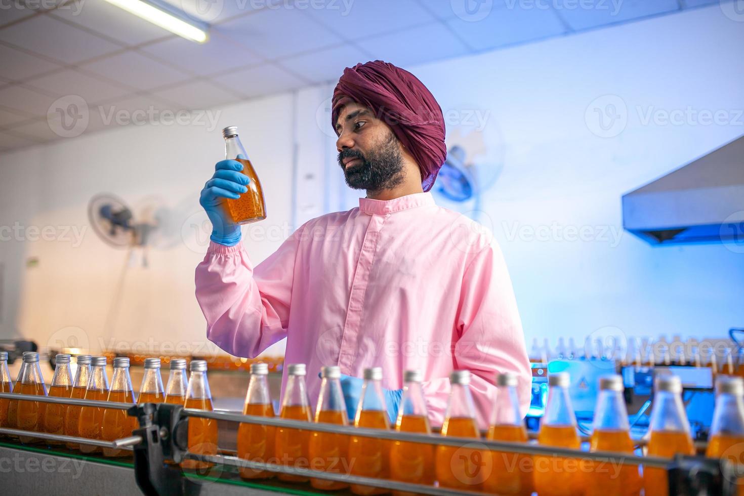 Asian man worker with clipboard is checking product bottles of fruit juice on the production line in the beverage factory. Manufacturer checks quality of food industry. photo
