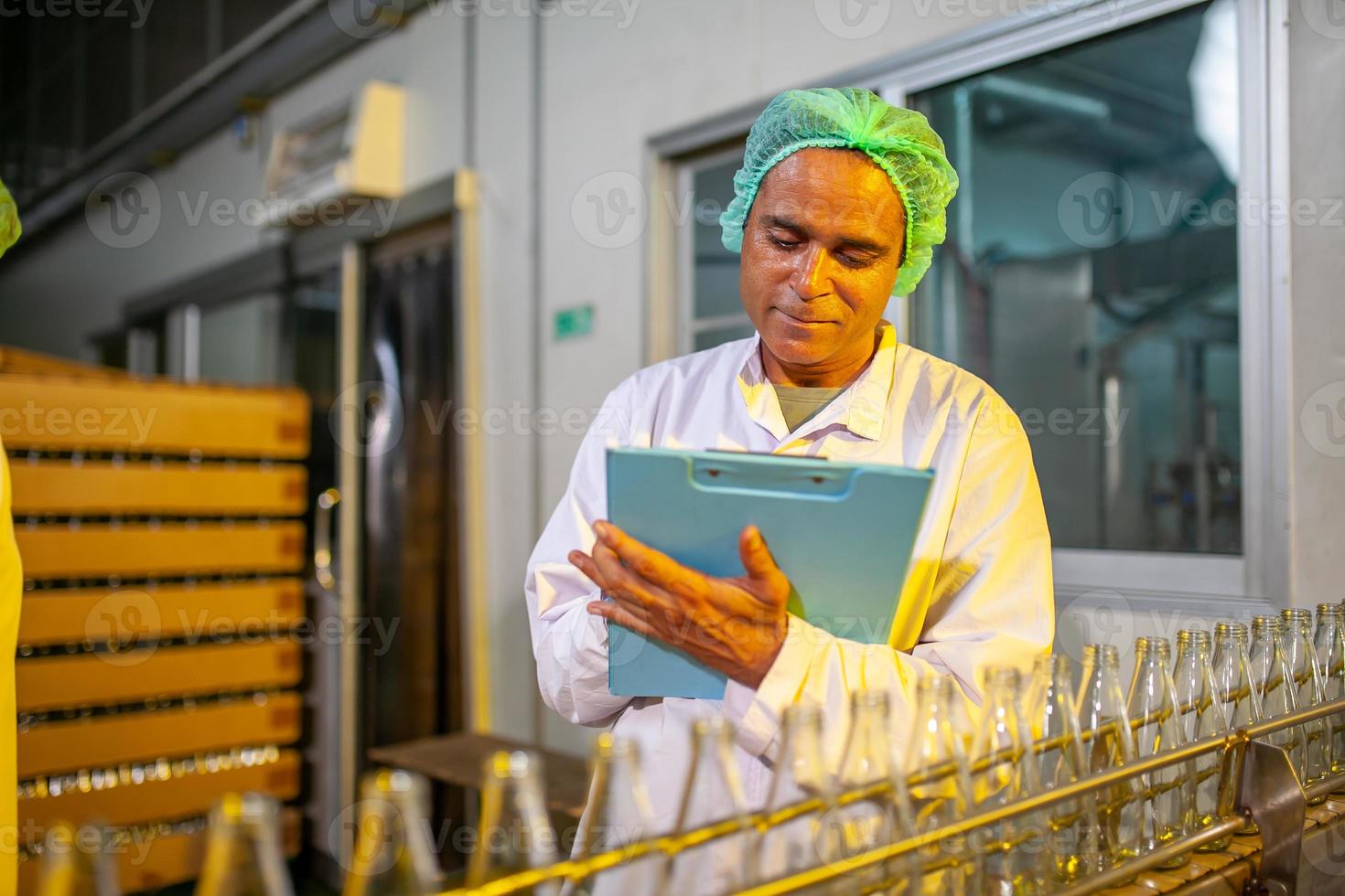 Asian workers with clipboard is checking product bottles of fruit juice on the production line in the beverage factory. Manufacturer checks quality of food industry. photo