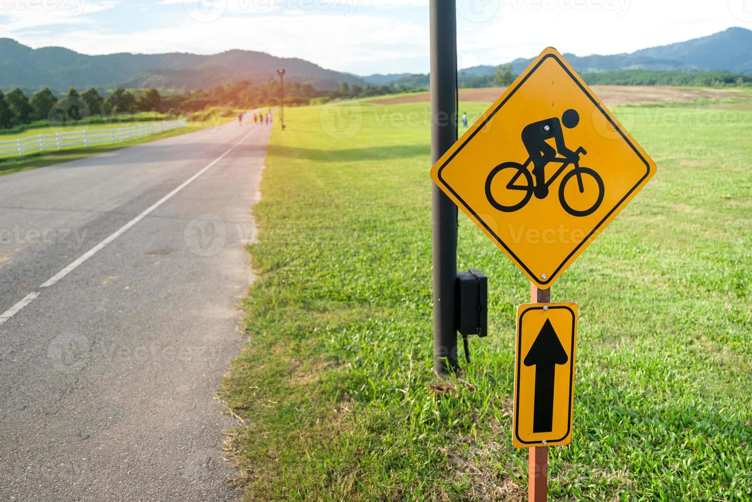 escénico del borde de la carretera del país con señal amarilla de carril bici y enorme campo de hierba verde. compartir el camino con los ciclistas sendero para andar en bicicleta concepto de señal de carretera de advertencia. foto