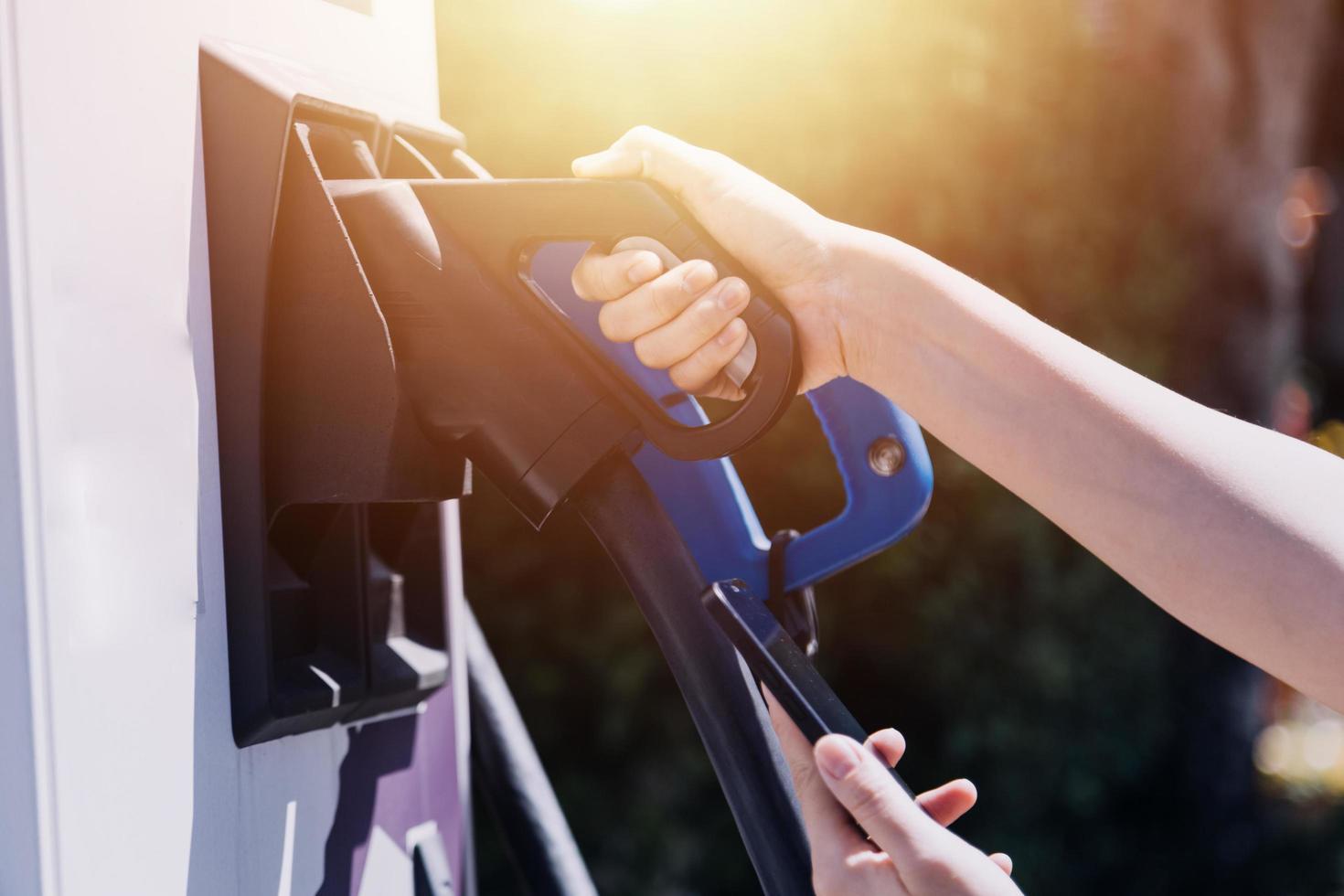 Hand plugging in a charger in an electric car socket.Electric car or ev is charging at station photo