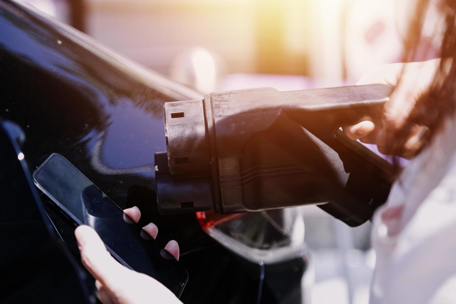 enchufar a mano un cargador en un enchufe de coche eléctrico.coche eléctrico o ev se está cargando en la estación foto