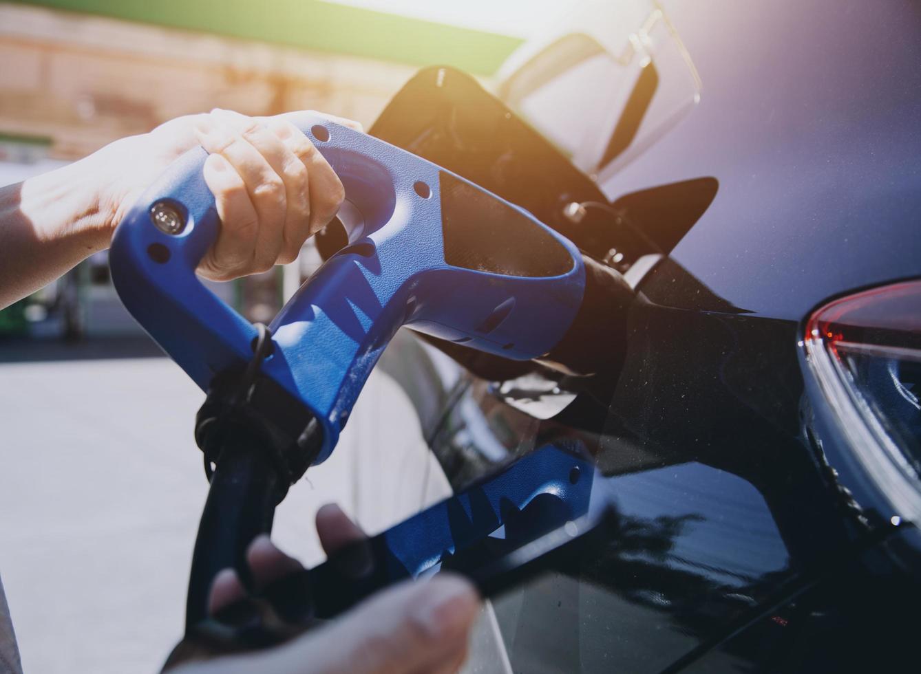 Hand plugging in a charger in an electric car socket.Electric car or ev is charging at station photo