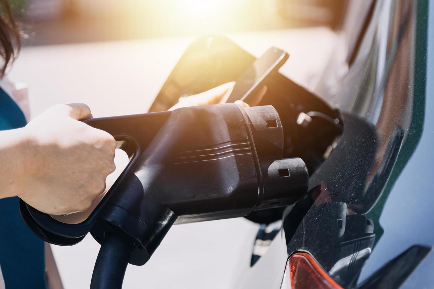 enchufar a mano un cargador en un enchufe de coche eléctrico.coche eléctrico o ev se está cargando en la estación foto