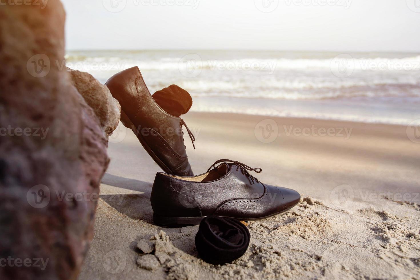 Work Life Balance Concept, Businessman take off his Working Oxford Shoes and leave it on the Sand Beach near the Rock for Walk into the Sea. Sky and Wave as background photo