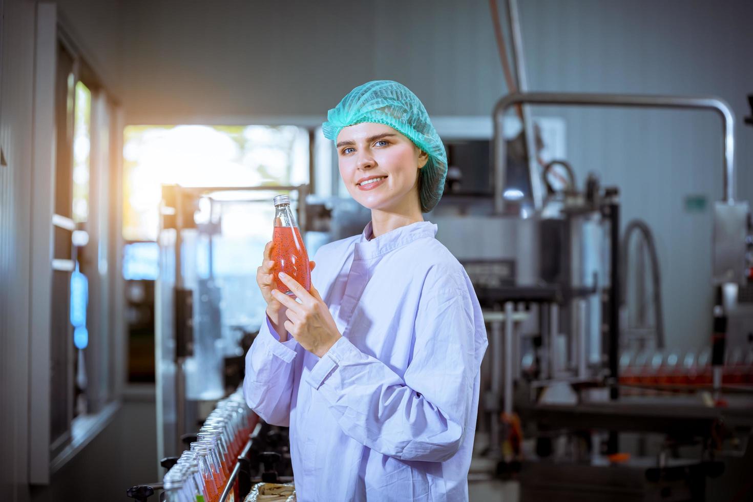 Worker of science in bottle beverage factory wearing safety hat posing show work to check quality of Basil seed produce on conveyer belt before distribution to market business. photo