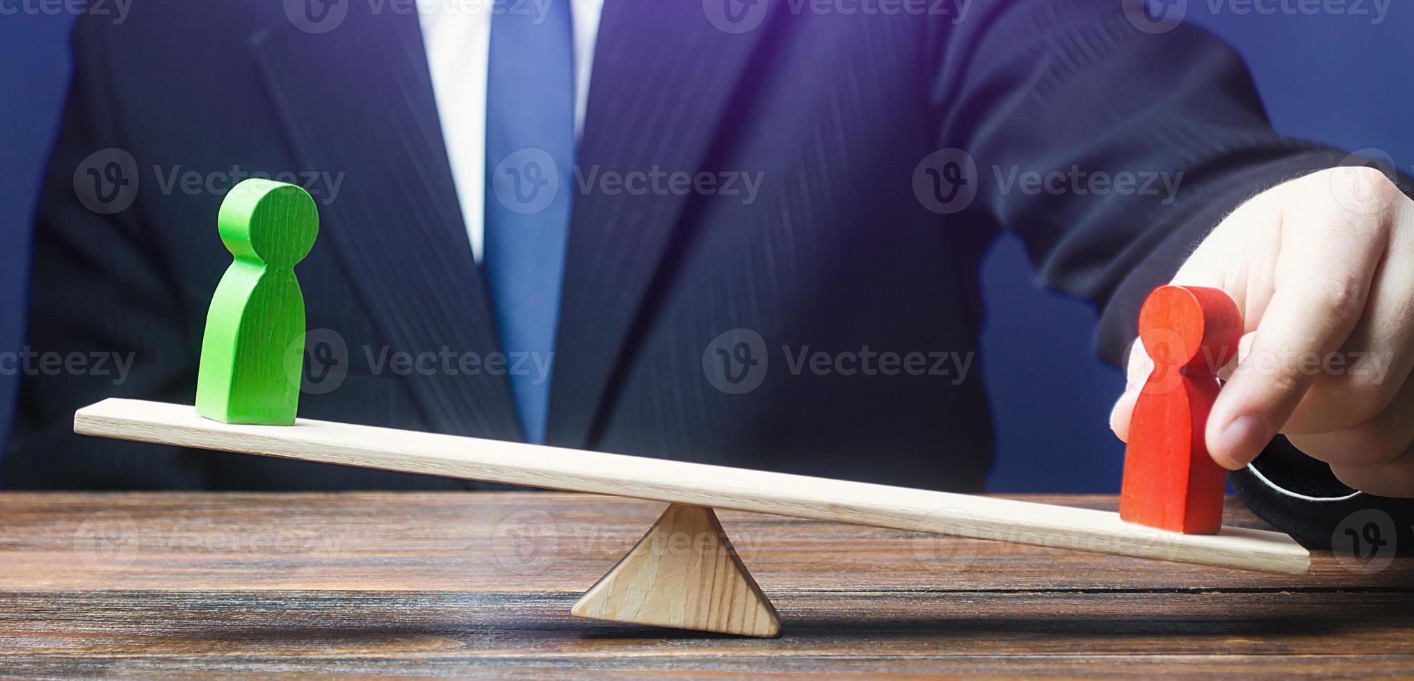 Man opposes green figure to red opponent on scales. Support enemy gain, Intrigue political struggle. Give an advantage, change balance of power, change outcome of confrontation. Invisible helping hand photo