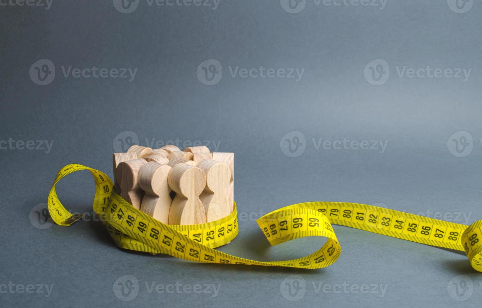 A crowd of wooden figures Gripped by measuring tape. Information statistics, measurement of the number, trends of population growth. Social Sciences. Promotion of ideas for weight loss, lifestyle photo