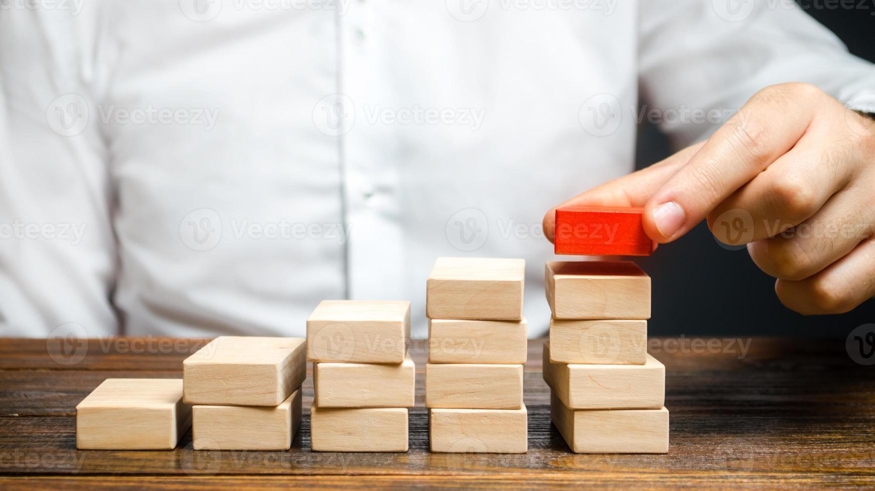 A man is building a ladder or growth chart from blocks. Strategy planning business expansion. Climbing the career ladder. Increase in income, organization of processors. Prioritization. Leadership photo