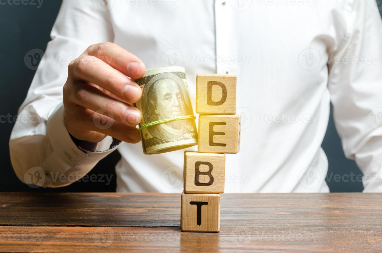 A man knocks down the tower with the word debt with the help of a bundle of money. Early repayment of the loan, remove interest charges and pay only the loan body. Exemption from microcredit. photo