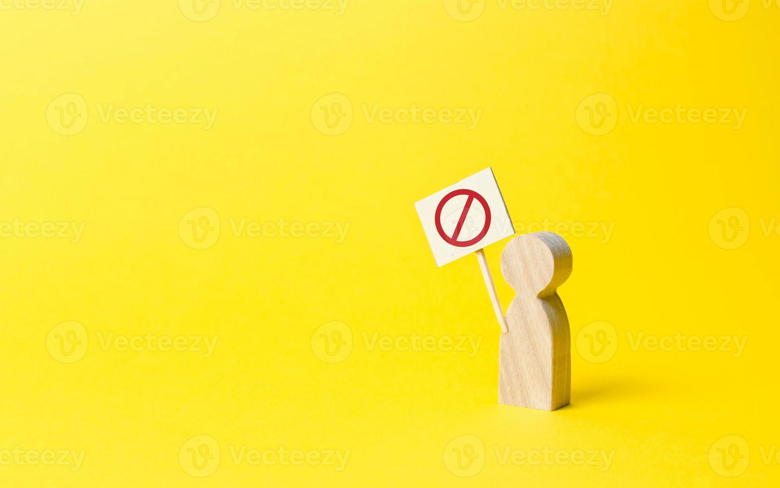 person figure with a sign with symbol NO on an yellow background. Social discontent and social tension, protest and disagreement. An angry wooden figure of people with a poster. photo