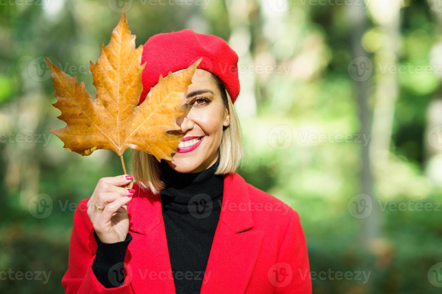 mujer sonriente cubriendo la cara con una hoja de arce foto