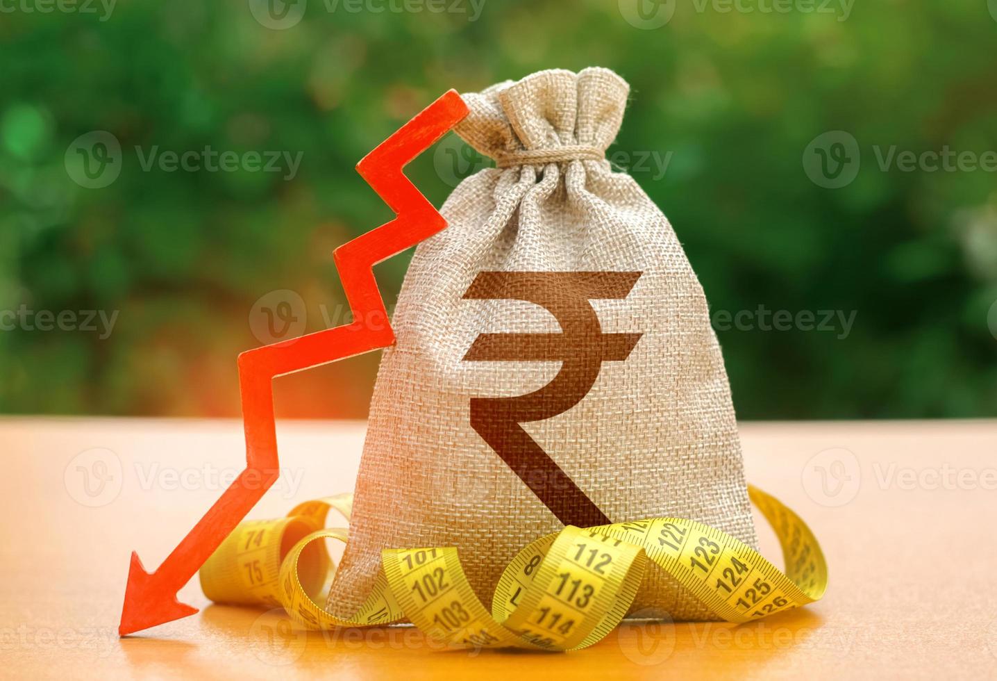 bolsa de dinero de la rupia india con flecha hacia abajo y cinta métrica. reducción de salarios, recortes en las prestaciones sociales. reducción de costos, ahorro. salida de capital. disminución de la tasa de descuento por parte del banco nacional. caída de salarios foto