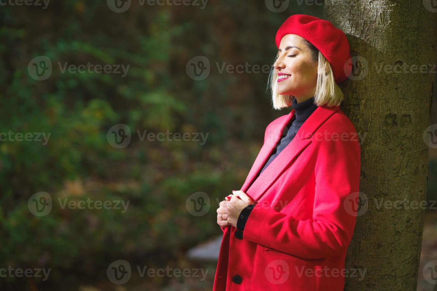 Gentle female wearing red beret and jacket standing near tree photo