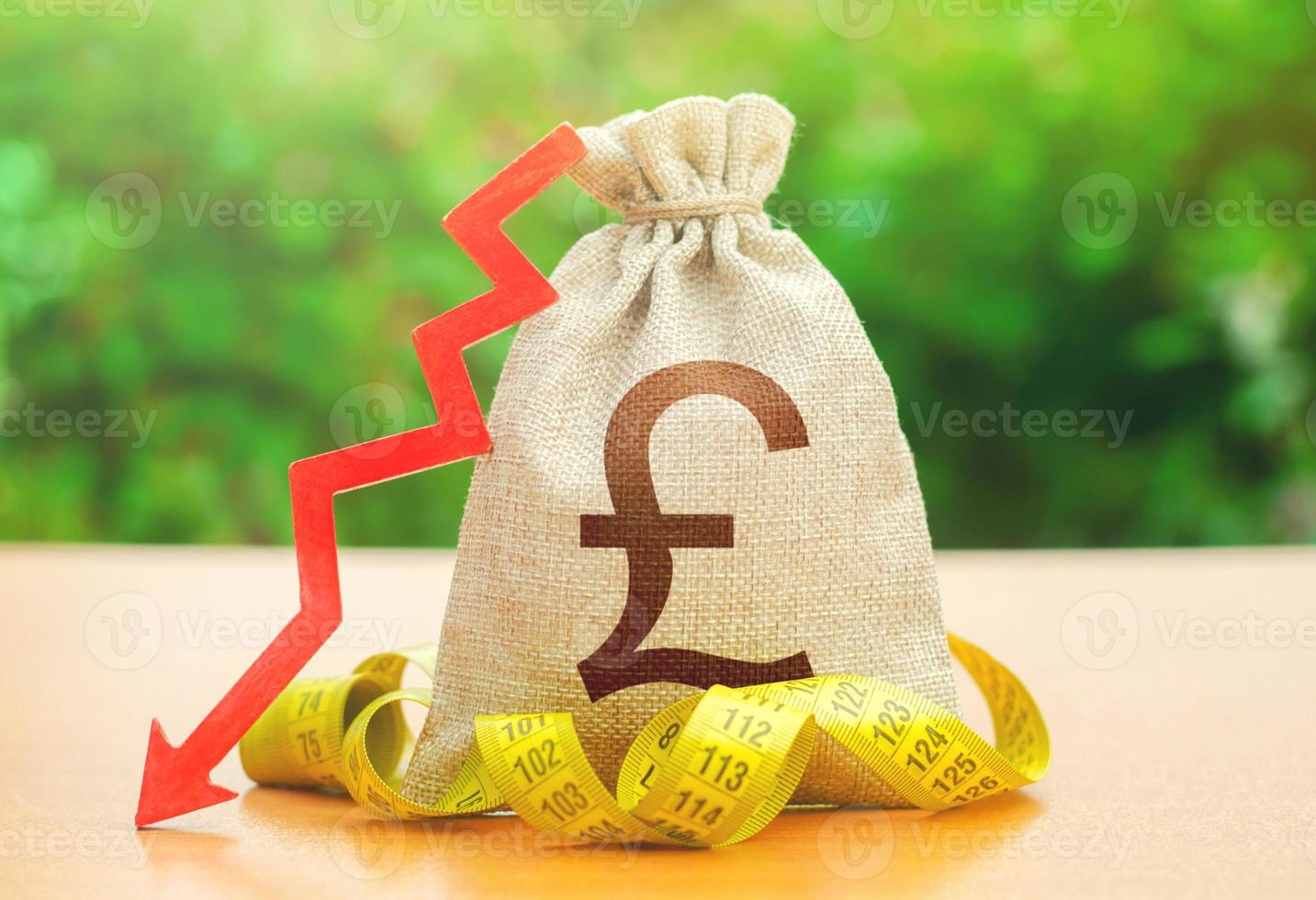 British pound sterling money bag with down arrow and measure tape. Falling wages and welfare. Reduced wages, cuts in social benefits. Cutting costs, saving. Capital outflow. Decrease in discount rate photo