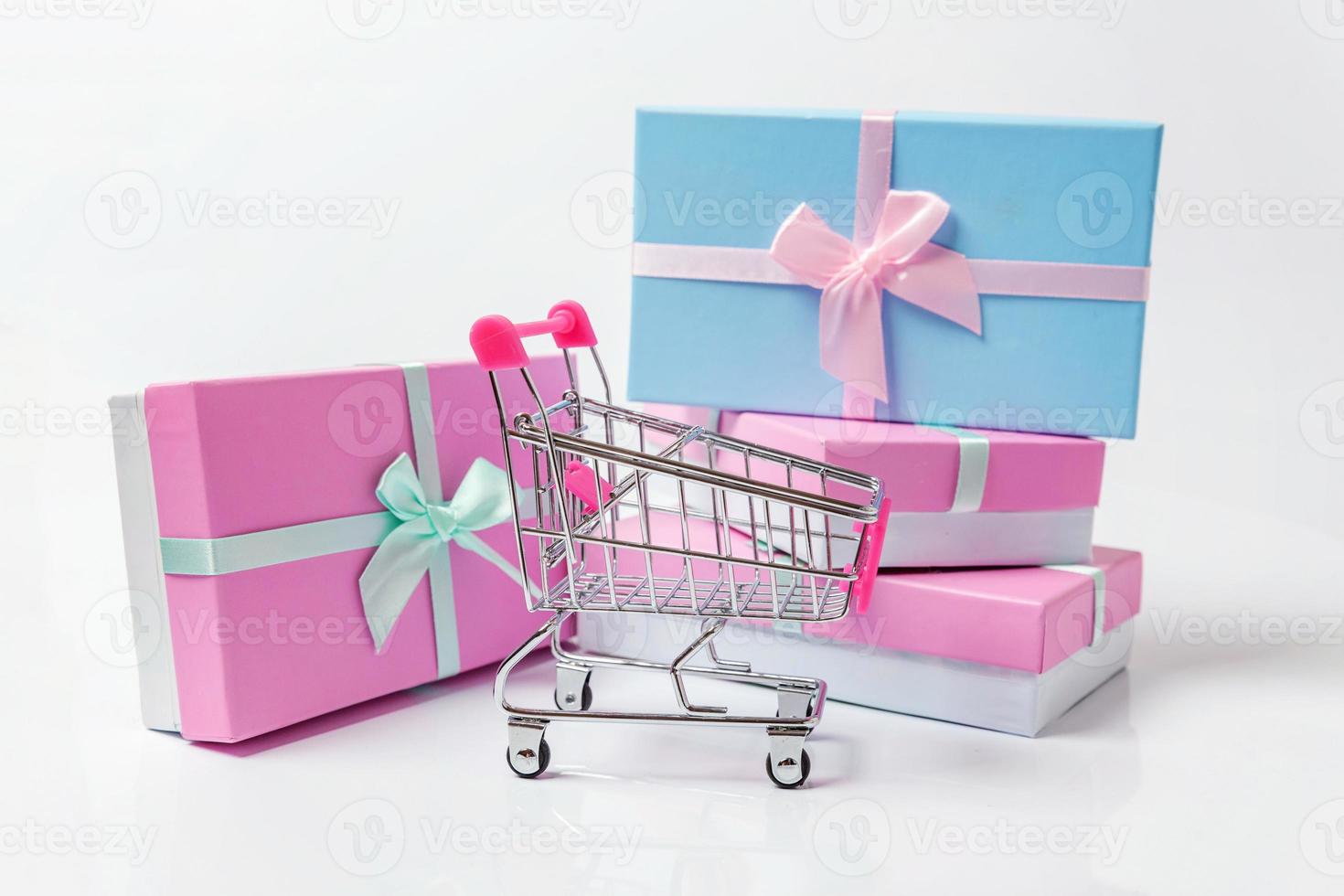 Small supermarket grocery push cart for shopping toy with blue, pink gift box isolated on white background. Sale buy mall market shop consumer concept. Copy space. photo