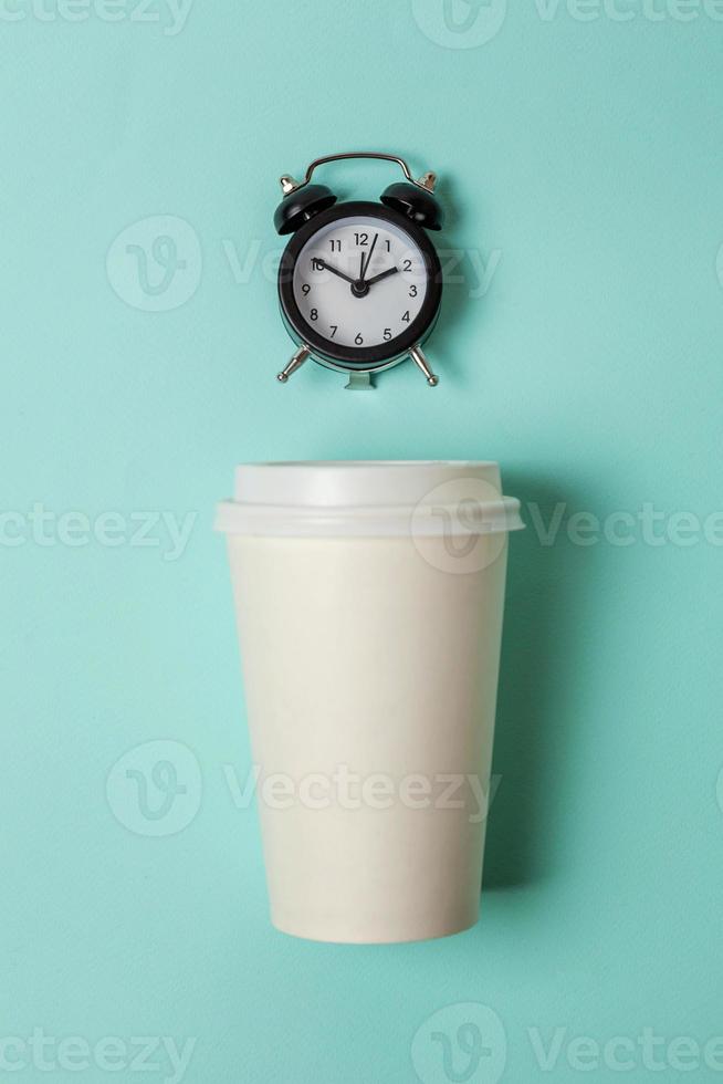 Simply flat lay design paper coffee cup and alarm clock on blue pastel colorful trendy background. Takeaway drink and breakfast beverage. Good morning wake up awake concept. Top view copy space. photo