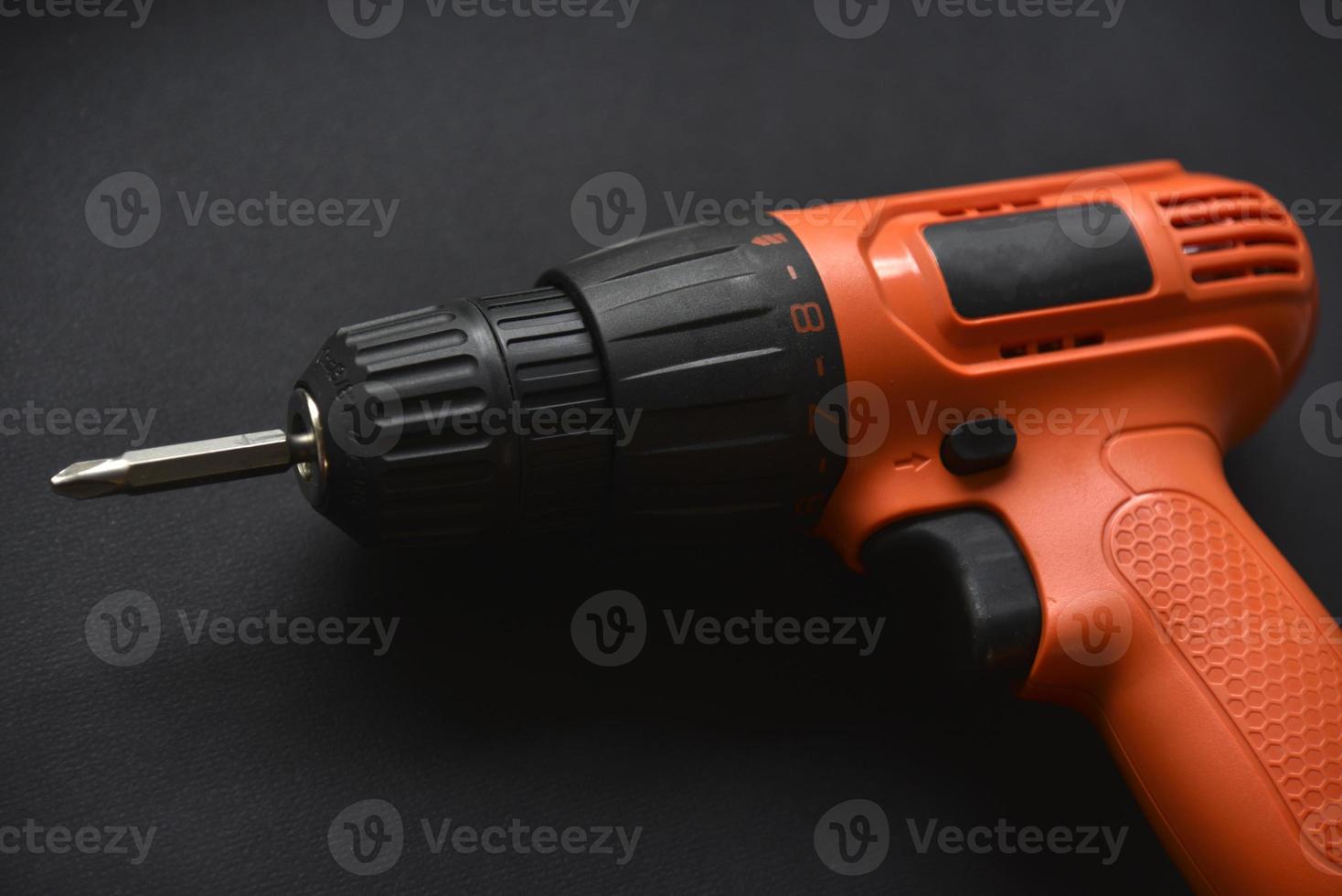 Orange screwdriver on a black background in the hand. Screwdriver and electric drill with power supply photo