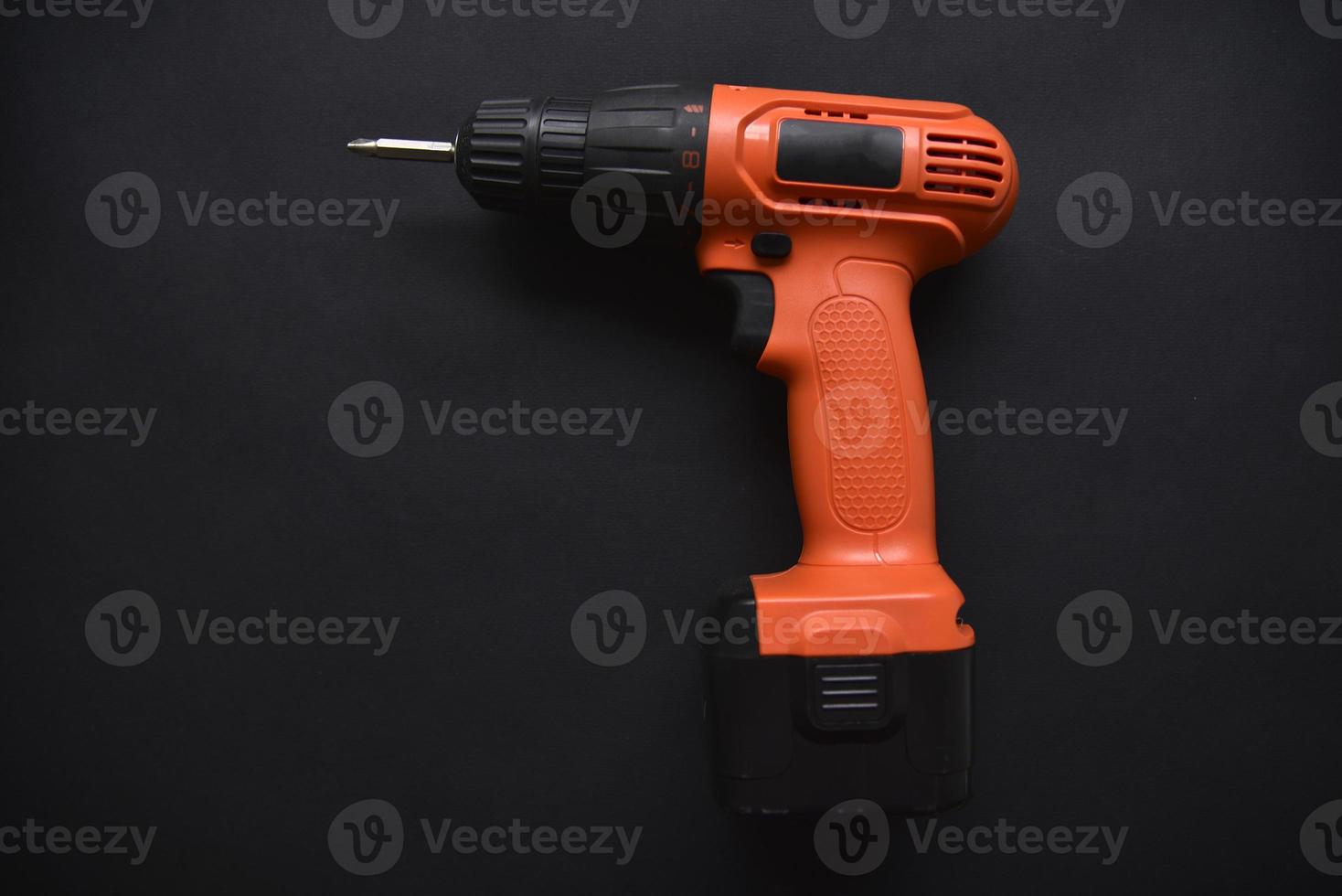 Orange screwdriver on a black background in the hand. Screwdriver and electric drill with power supply photo
