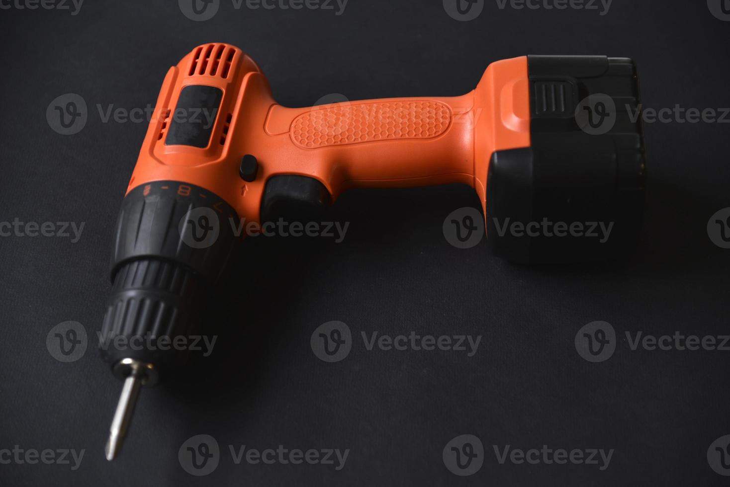 Orange screwdriver on a black background in the hand. Screwdriver and electric drill with power supply photo