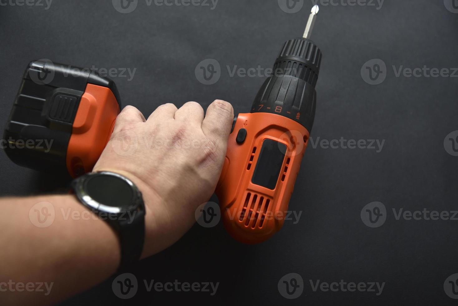 Orange screwdriver on a black background in the hand. Screwdriver and electric drill with power supply photo