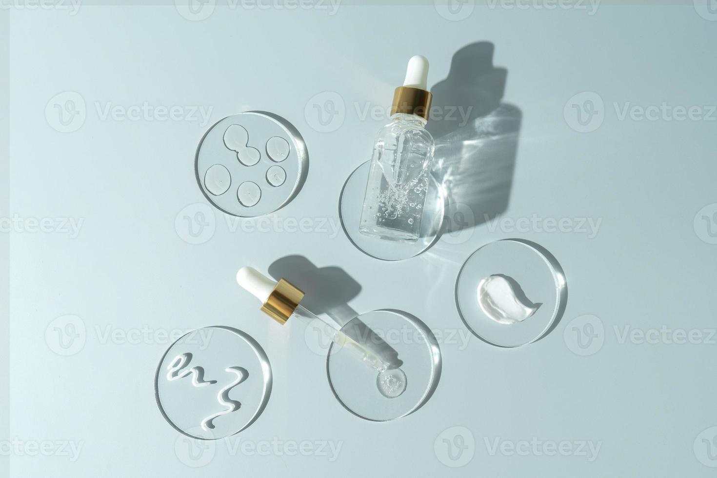 A transparent face serum or oil in a dropper bottle with drops on a round podiums. Cosmetology and pharmaceuticals concept. photo