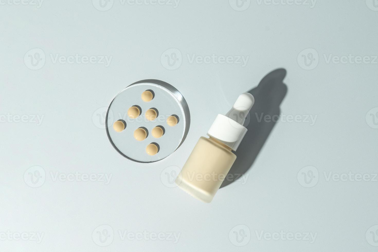 A face tonal cream in a dropper bottle and drops of the cream on a glass plate. Cosmetology and makeup concept photo
