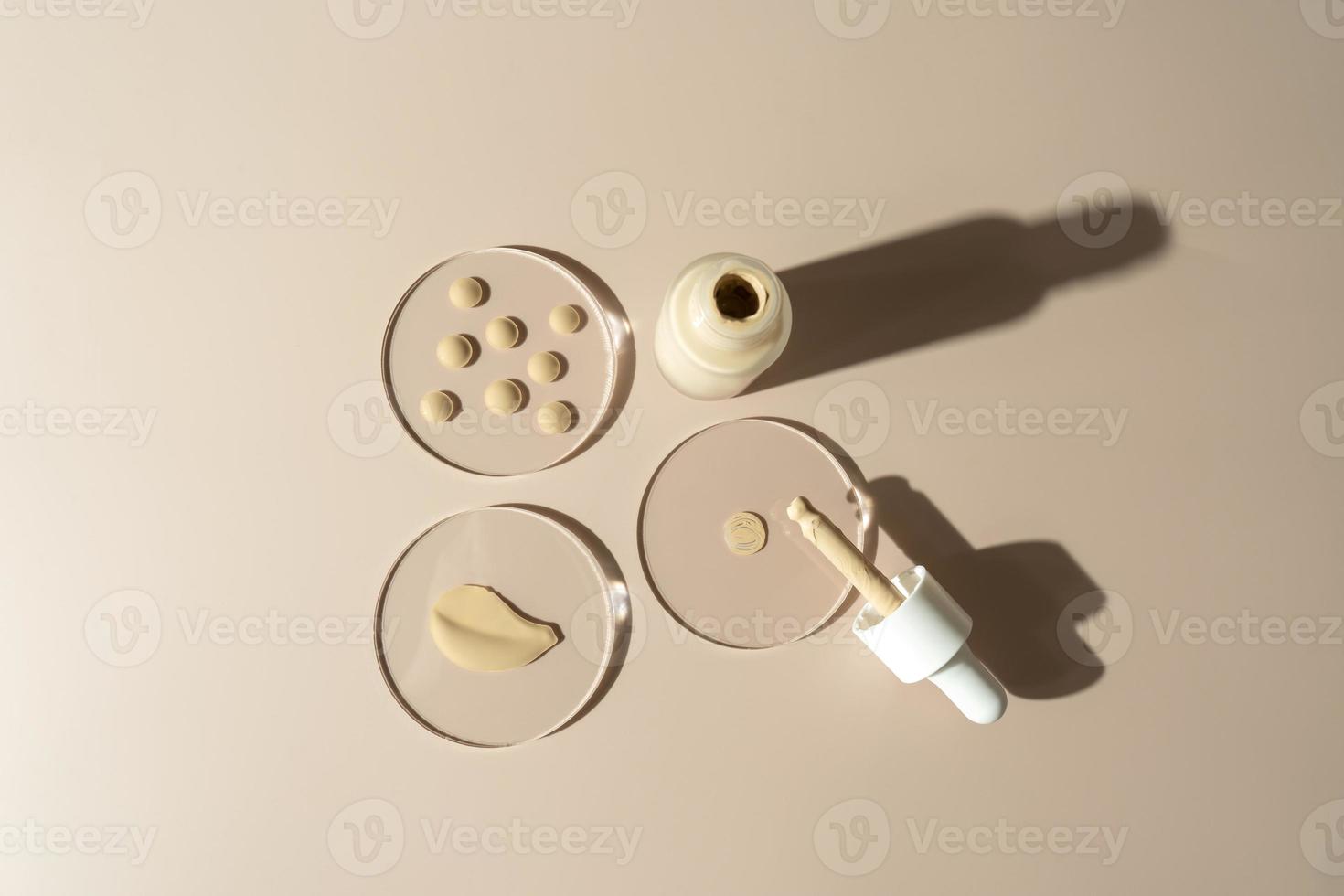 A face tonal cream in a dropper bottle and drops of the cream on a glass plate. Cosmetology and makeup concept photo