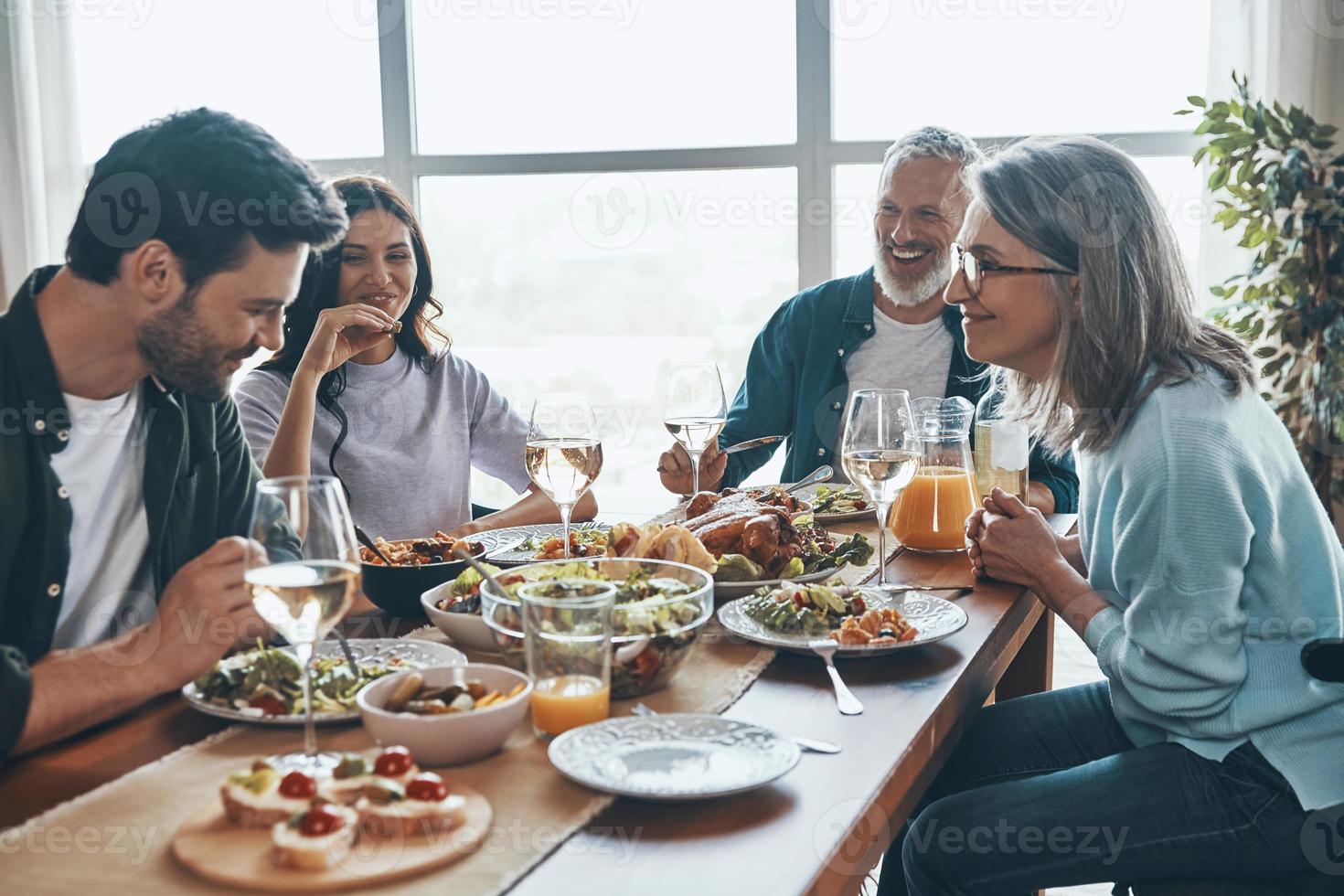 feliz familia multigeneracional comunicándose y sonriendo mientras cenamos juntos foto