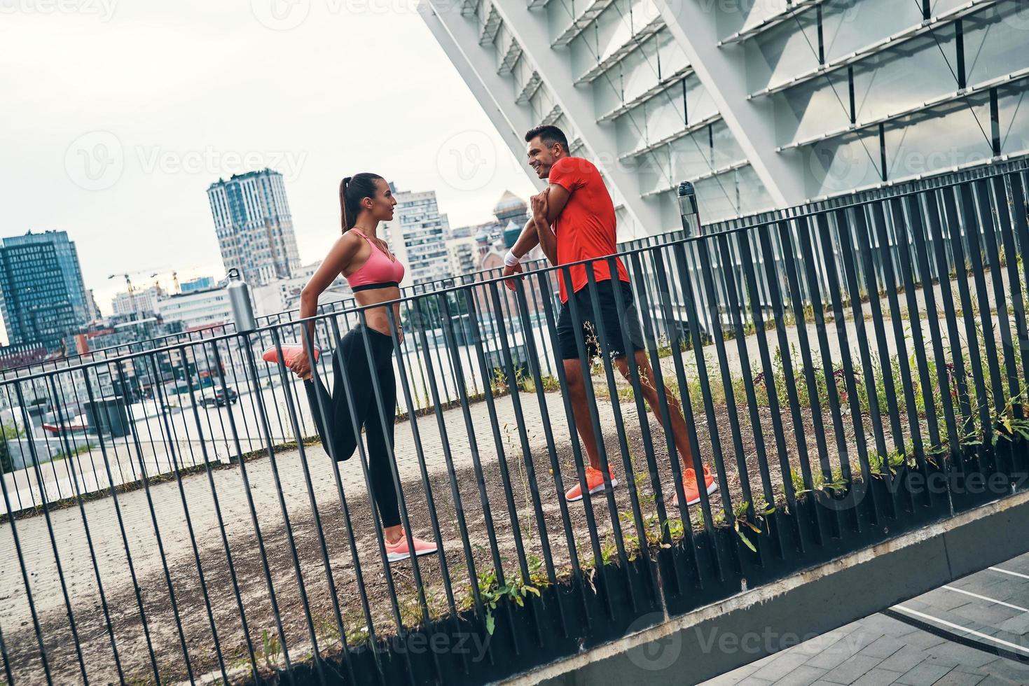 Full length of self-motivated young couple in sports clothing warming up and stretching while practicing outdoors on the city street photo