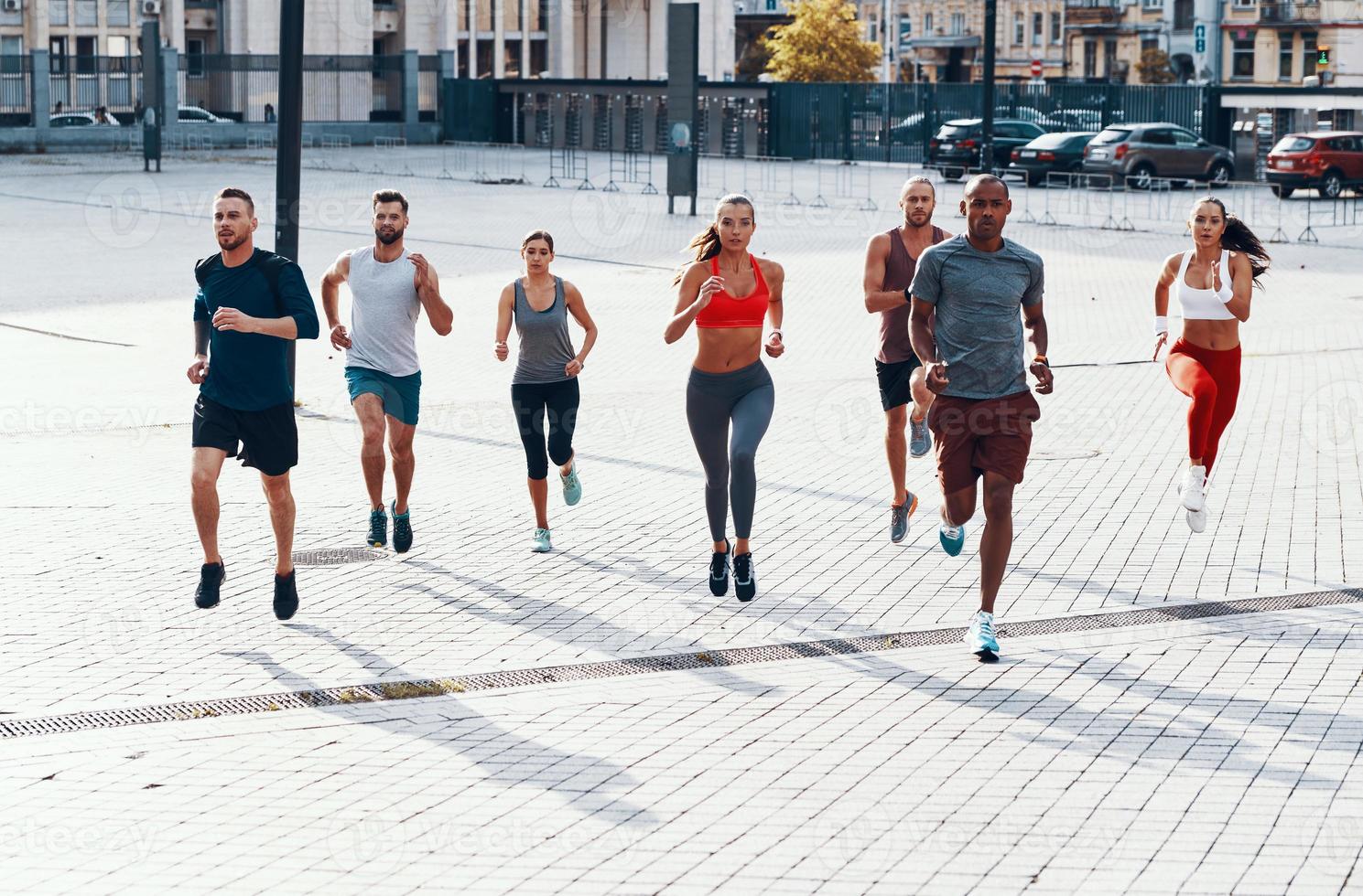 Full length of people in sports clothing jogging while exercising on the sidewalk outdoors photo