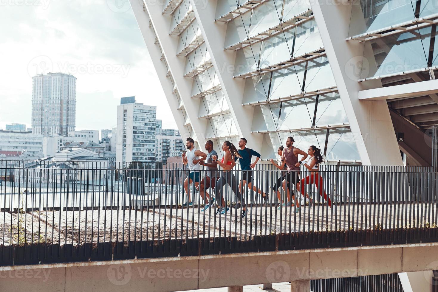 Full length of young people in sports clothing jogging while exercising on the bridge outdoors photo