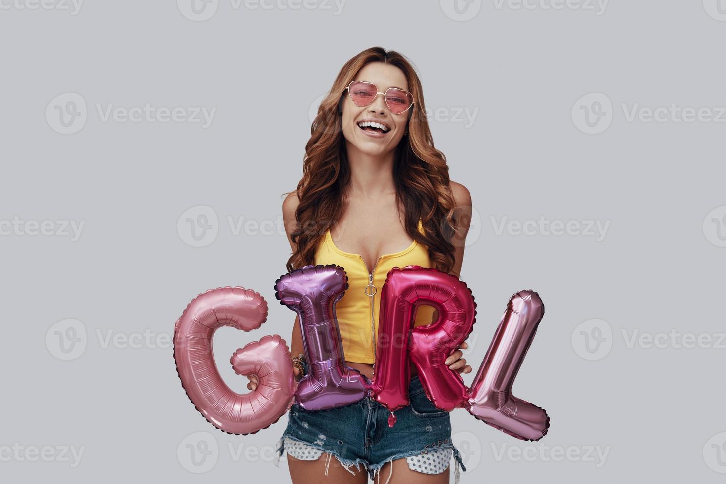 Attractive young woman looking at camera and smiling while standing against grey background photo