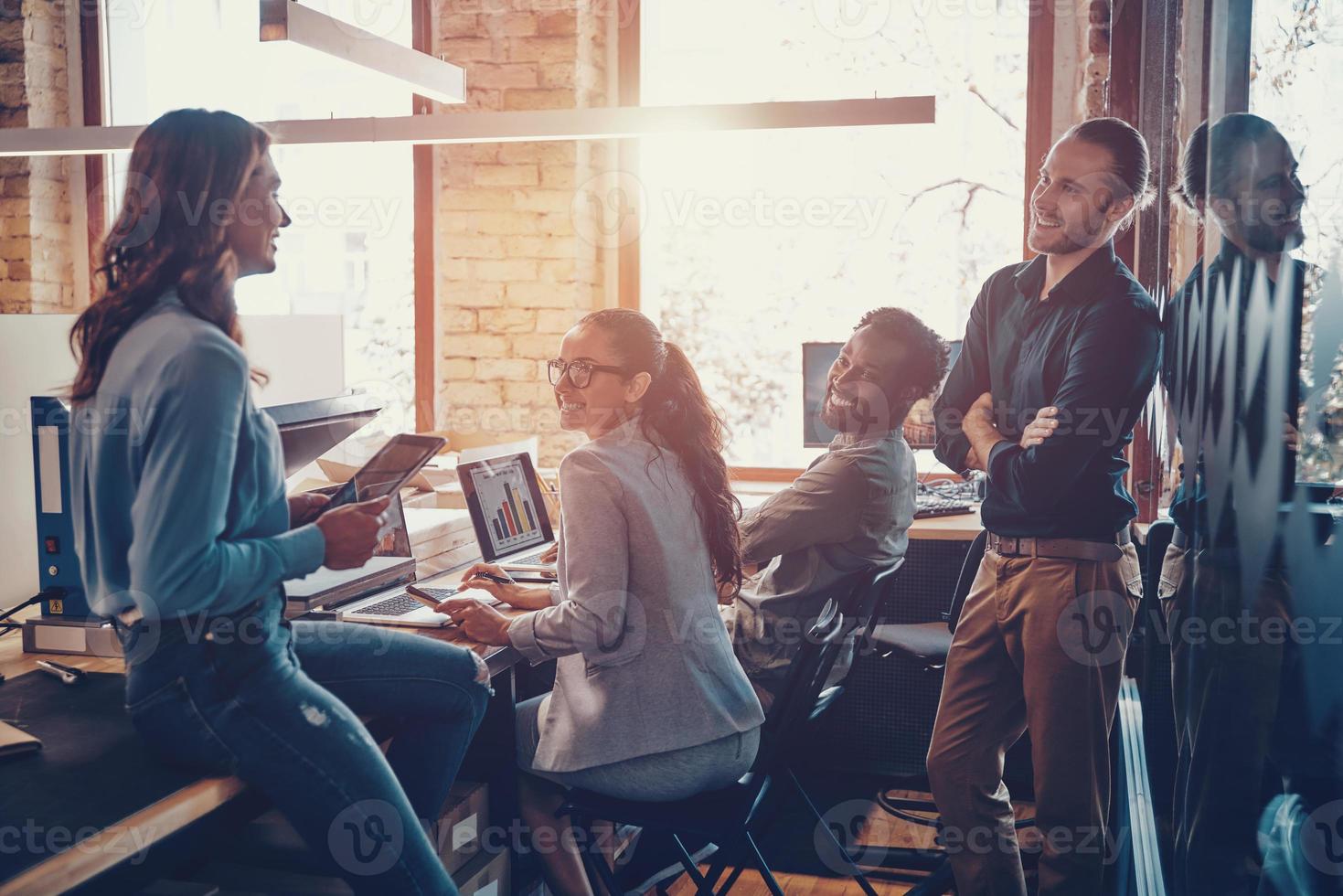 Group of young modern people in smart casual wear communicating and using modern technologies while working in the office photo