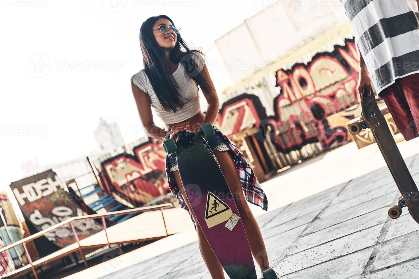 Simply happy. Beautiful young woman smiling while leaning on the skateboard outdoors photo