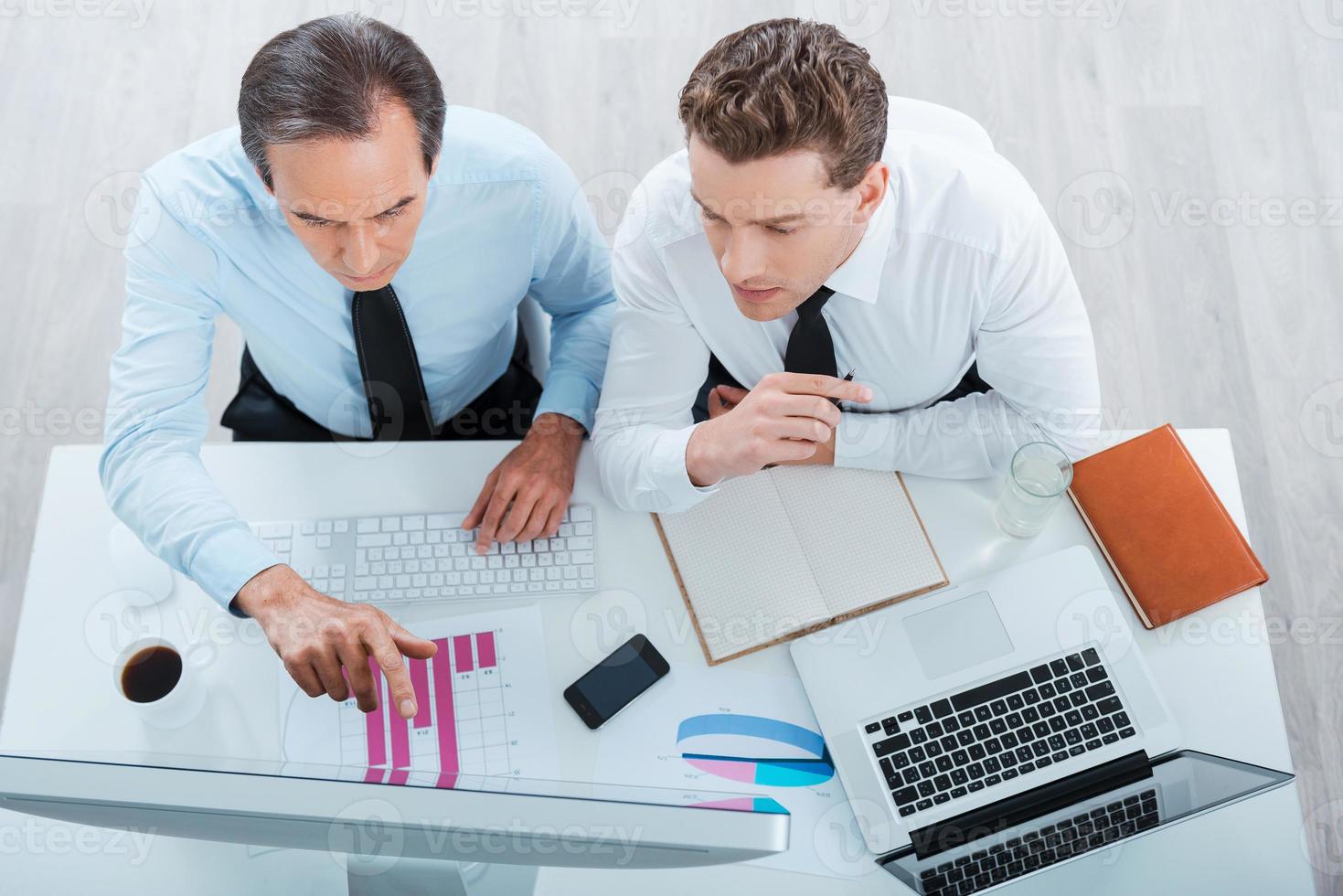 encontrar soluciones juntos. vista superior de dos empresarios concentrados en ropa formal trabajando y mirando la computadora mientras están sentados en el lugar de trabajo foto