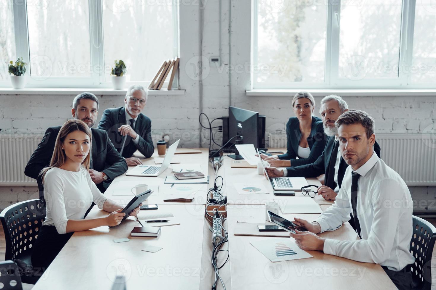 Group of people in elegant formalwear looking at camera and using modern technologies while working in the office photo