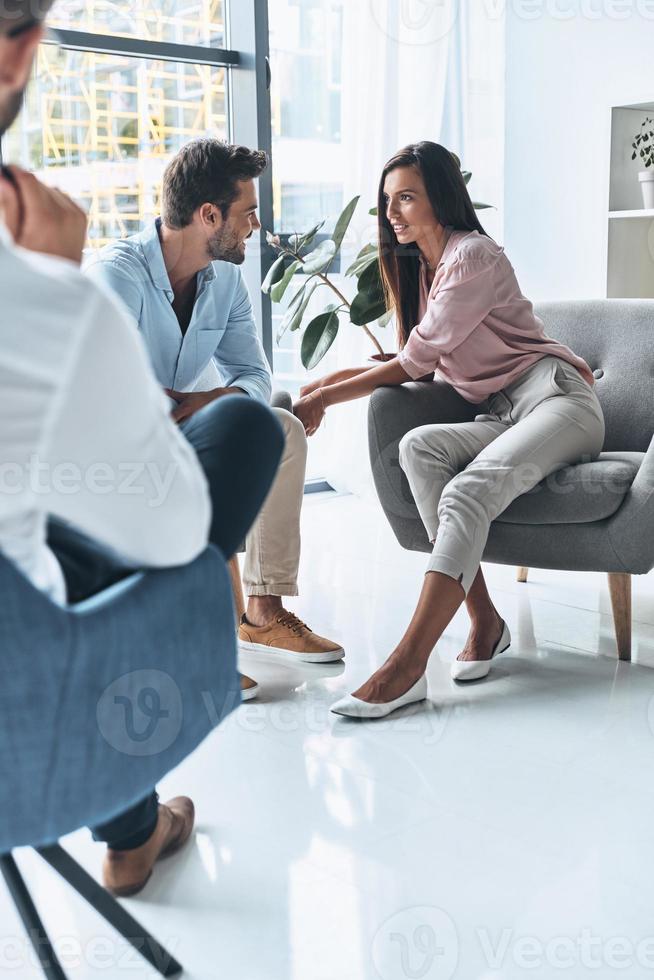 Good session. Young married couple talking and smiling while sitting on the therapy session with psychologist photo