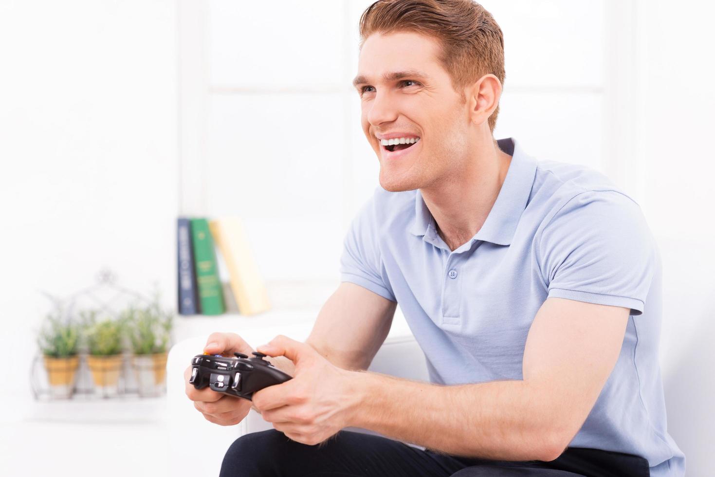 Playing his favorite video game. Happy young man using joystick while playing video game at home photo