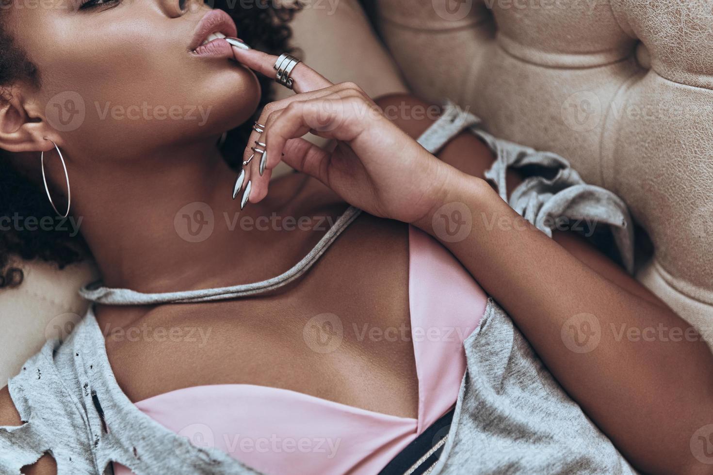 Extremely sensual. Close-up top view of attractive young African woman touching her lip with finger while lying on the sofa at home photo