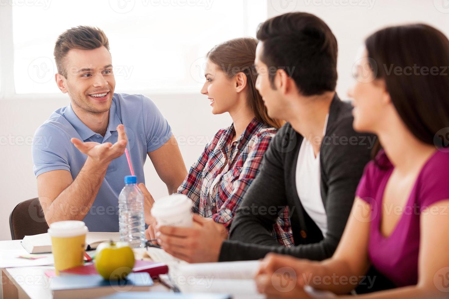 Students meeting. Four cheerful students talking to each other while sitting at the desk photo