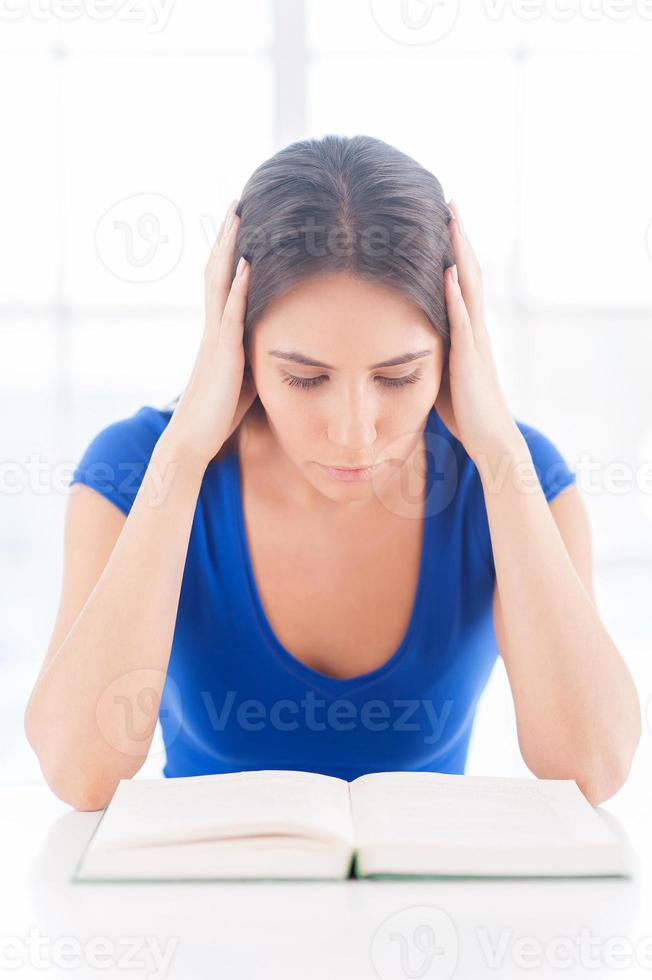 Reading a boring book. Frustrated young woman reading a book and holding head in hands photo
