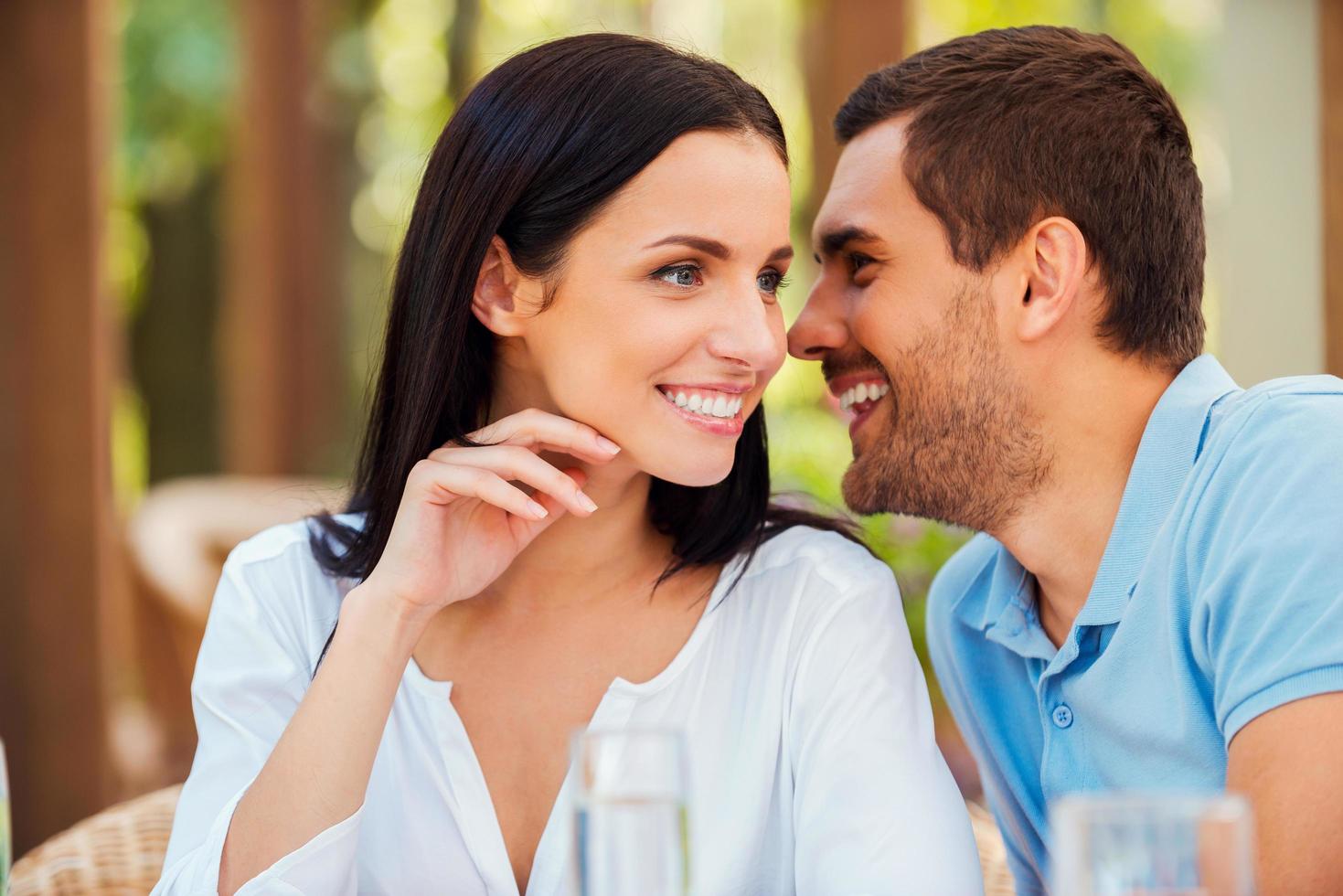 compartir secretos con ella. un joven apuesto que le dice algo a su novia y sonríe mientras se sienta en la mesa al aire libre juntos foto