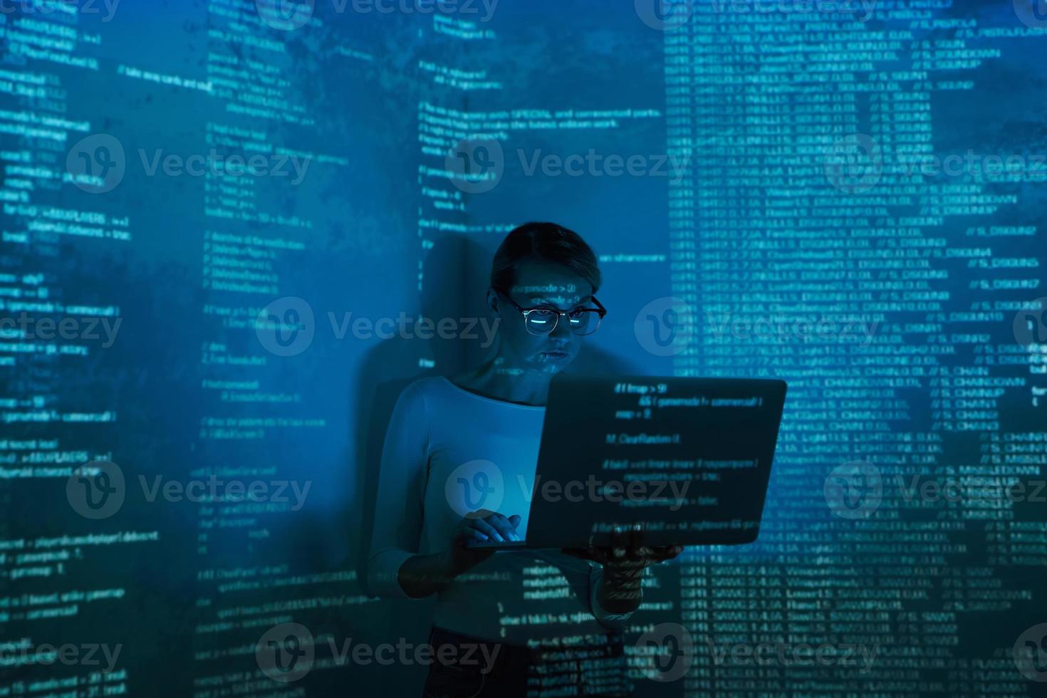 Confident young woman using computer against dark background photo