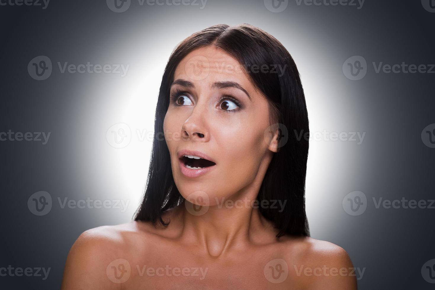 Feeling terrified. Portrait of shocked young shirtless woman looking away and keeping mouth open while standing against grey background photo