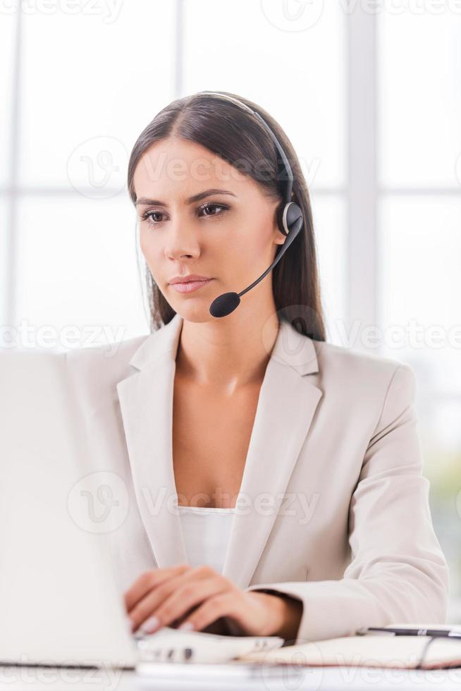 Supporting your business. Beautiful young businesswoman in headset using computer while sitting at her working place photo