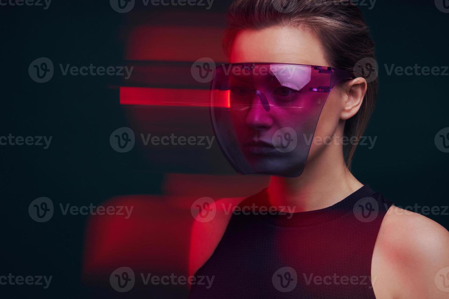 Confident young woman wearing futuristic glasses against dark background photo